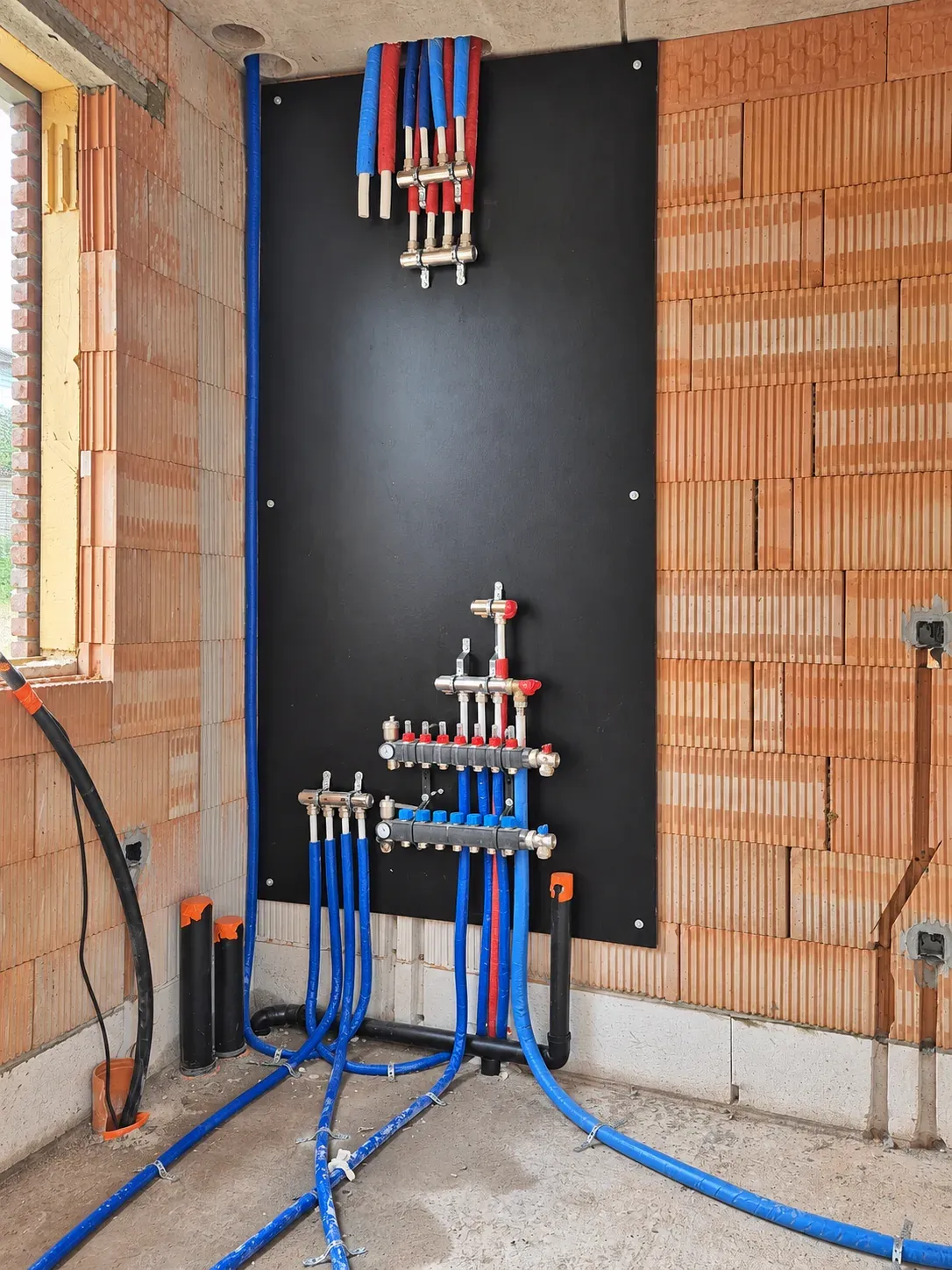 Verdeelcollectoren met blauwe en rode leidingen op een technische wand in ruwbouw