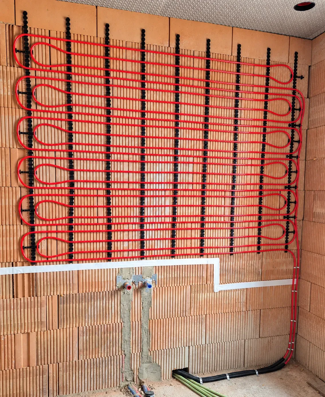 Wandverwarmingsbuizen in rode lussen op een bakstenen badkamermuur, voor de bepleistering